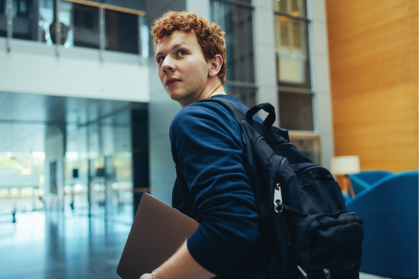 Un jeune diplômé sort de cours en tenant son ordinateur